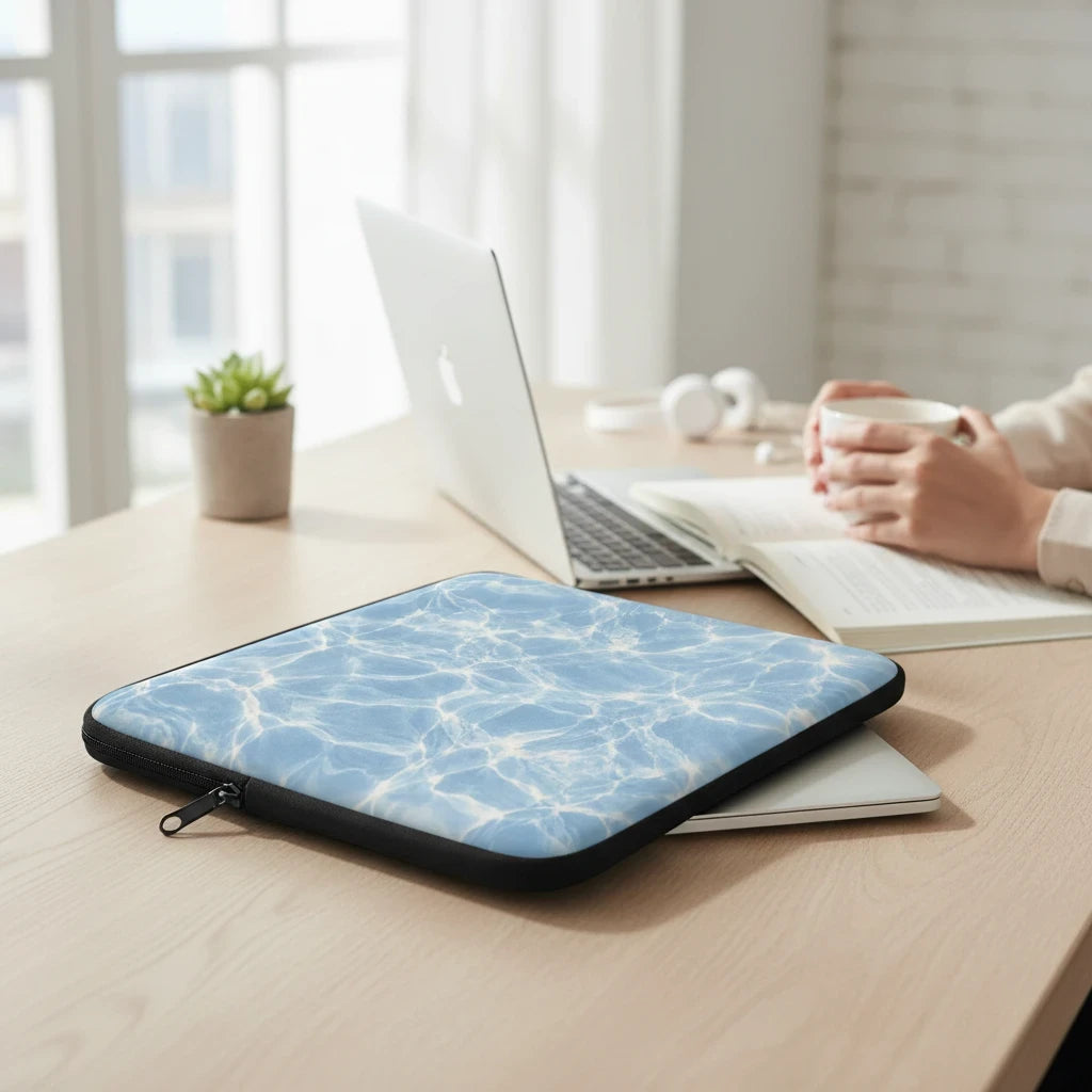 Sunday Theory blue water ripple print laptop sleeve with plush fleece interior on a wooden desk near a laptop.