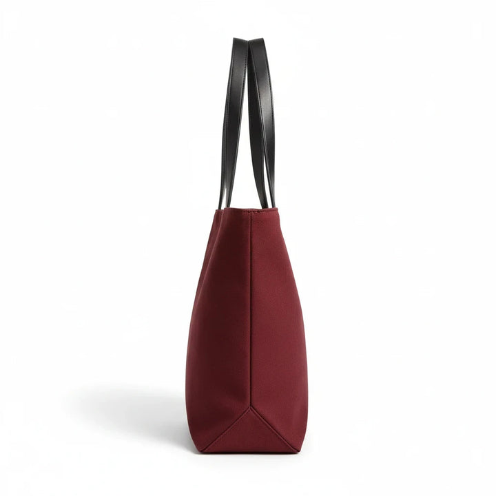 Sunday Theory burgundy canvas tote bag with black leatherette handles, side profile view on a white background.
