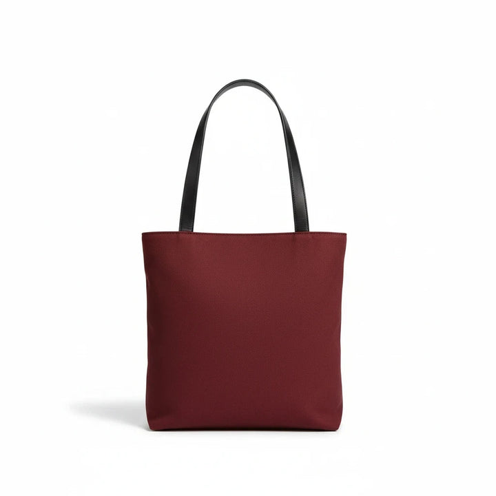 Sunday Theory burgundy canvas everyday tote bag with black shoulder straps against a plain white background