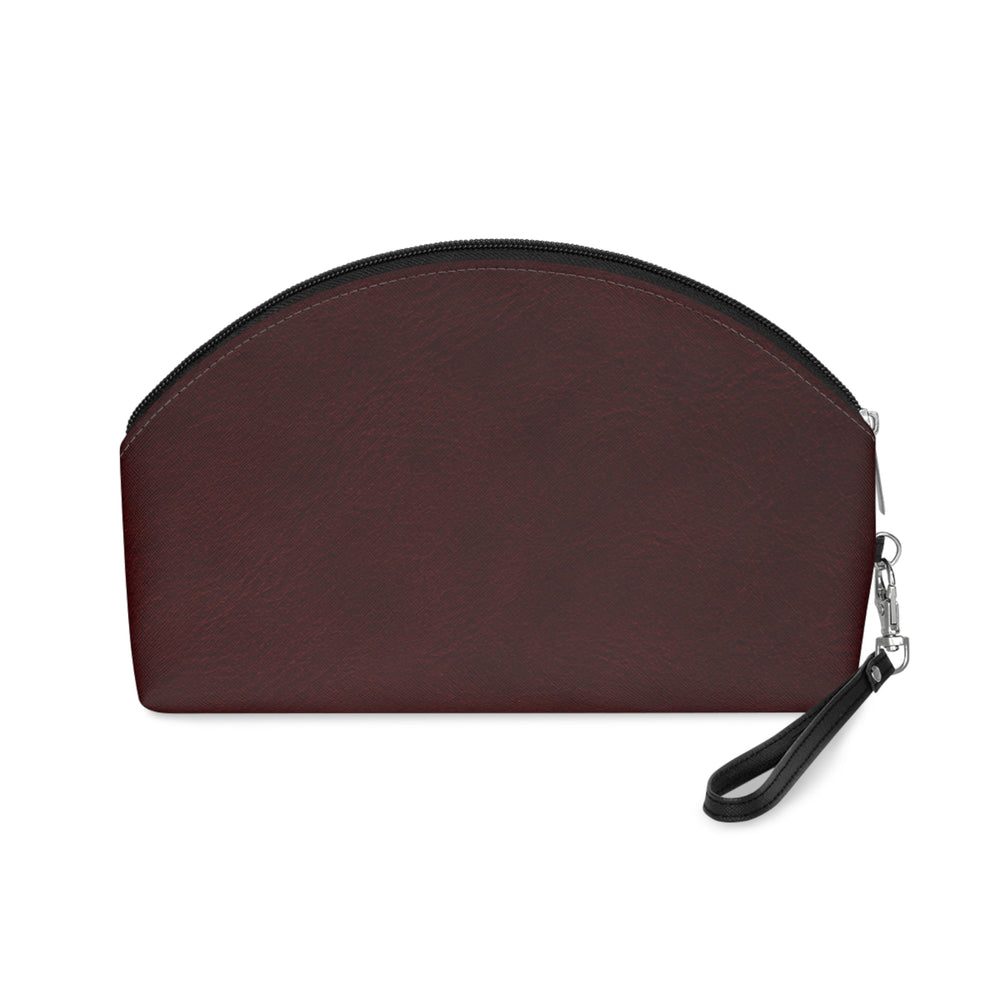 Sunday Theory burgundy faux leather makeup bag with a curved silhouette, black zipper, and detachable wrist strap.