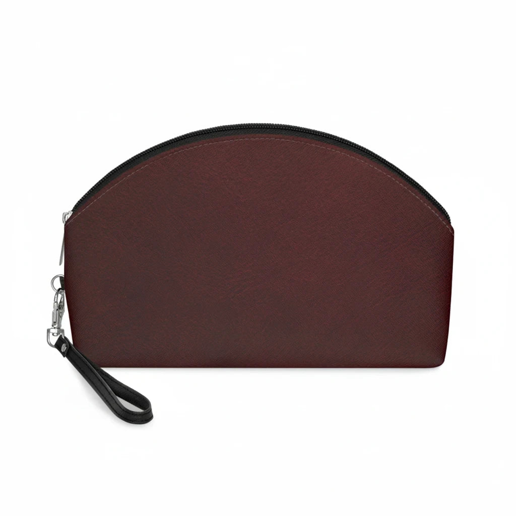 Sunday Theory burgundy faux leather makeup bag with a curved shape, black zipper, and a detachable wrist strap.