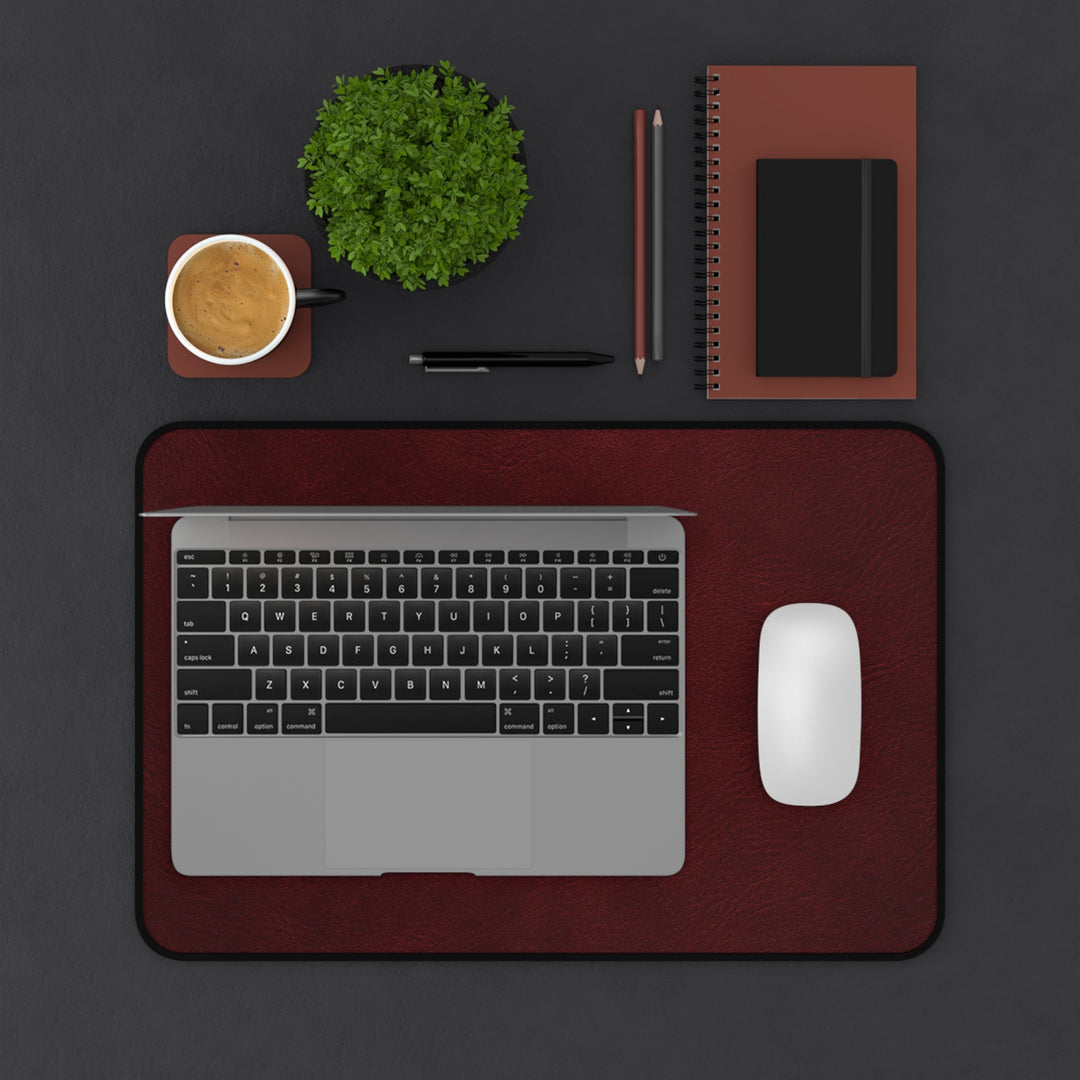 Sunday Theory burgundy leather-look neoprene desk mat with a laptop and mouse on a dark office workspace desk