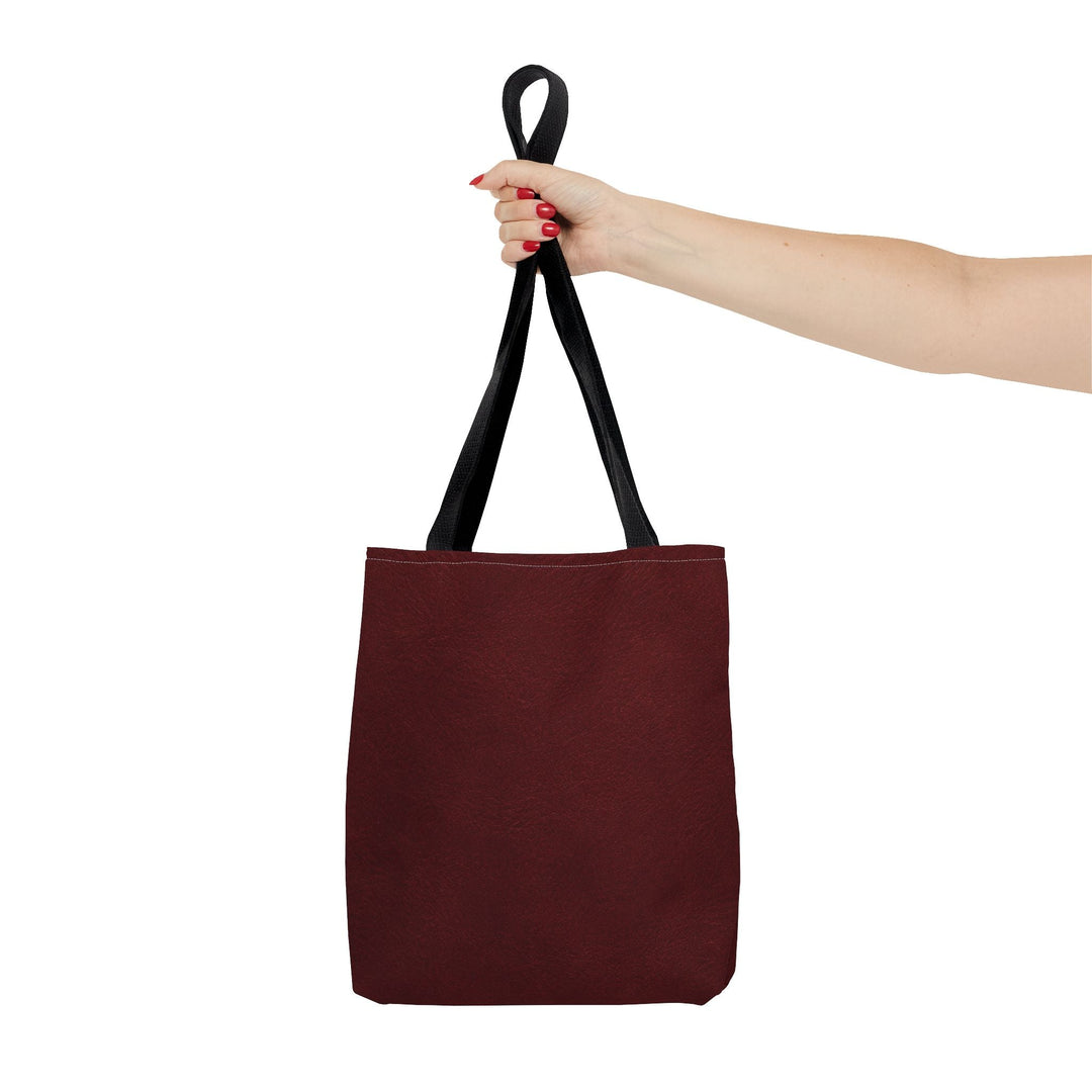 Sunday Theory burgundy polyester everyday tote bag with black cotton handles held by a hand against a white background