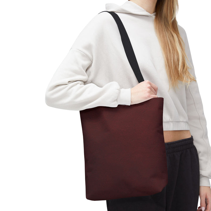 Sunday Theory burgundy polyester everyday tote bag with black cotton handles worn over the shoulder by a model.