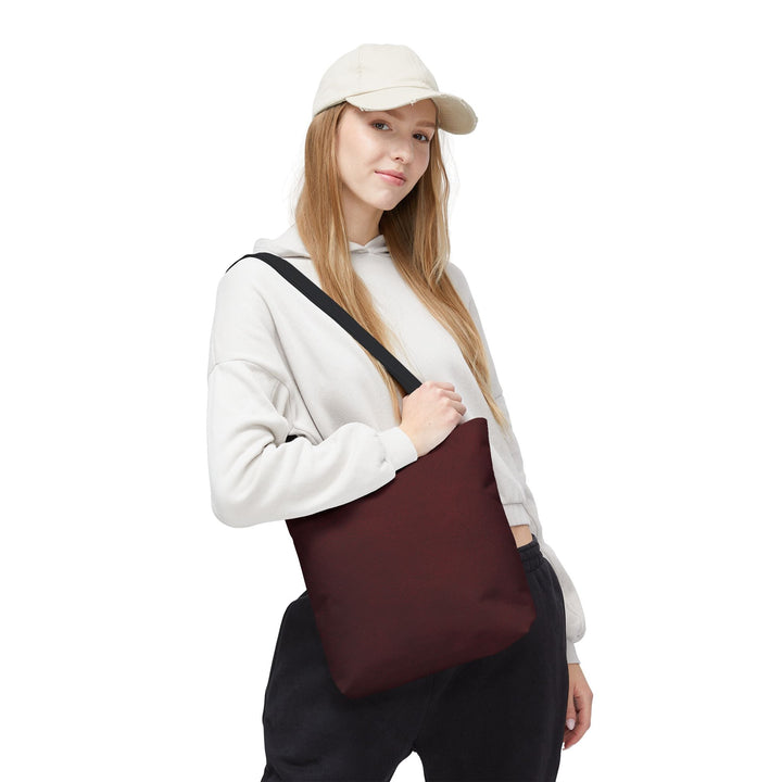 Sunday Theory burgundy polyester everyday tote bag with black handles worn over the shoulder by a woman in a hoodie