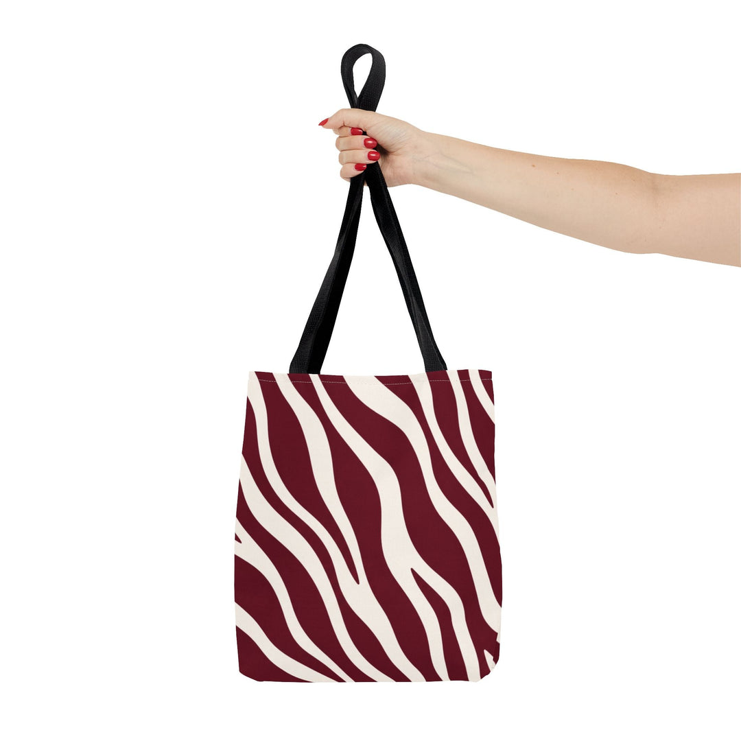 Sunday Theory maroon and cream zebra print polyester tote bag with black handles held by a hand against white.