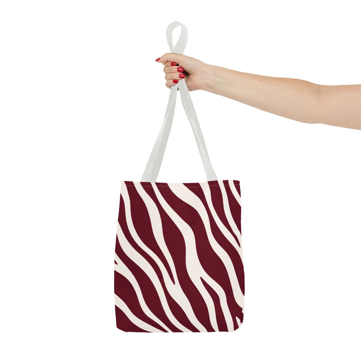 Sunday Theory maroon and cream zebra print tote bag held by a hand with red nail polish against a white background