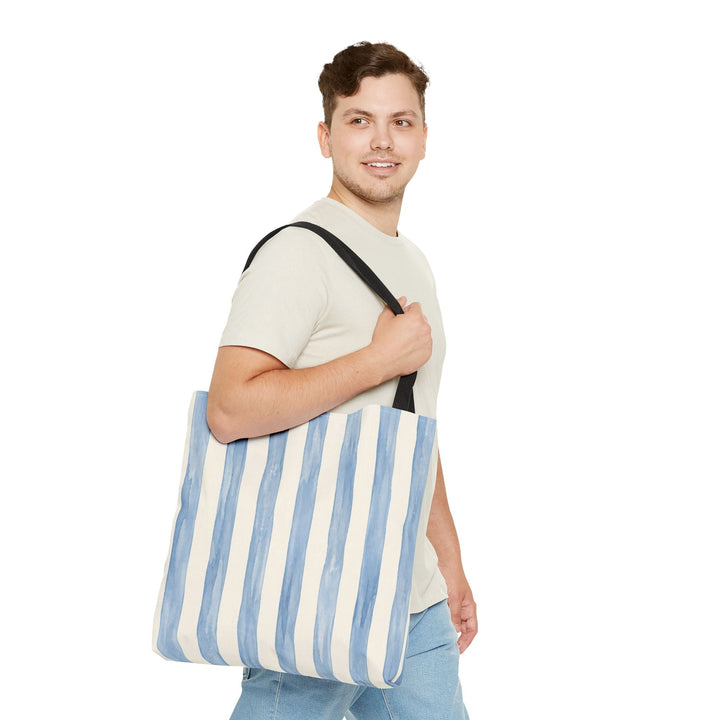 Sunday Theory striped blue watercolor canvas tote bag with black handles worn over the shoulder by a smiling man